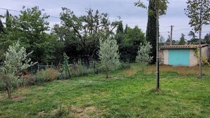 A grassy area with trees and a small building with a blue door. - Quiet, detached house close to shops and hiking trails. (Forcalquier)