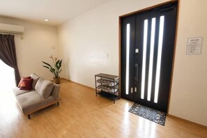 Un salon comprenant un canapé, une plante, un meuble à chaussures et une porte dotée de bandes lumineuses verticales.