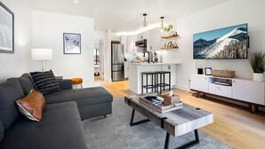 A modern living room with a grey sofa, a coffee table, and a kitchen in the background. - West Side Chic: A Light & Bright Ski Retreat (Telluride)