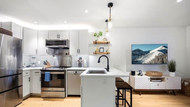 A modern kitchen with white cabinetry, stainless steel appliances, a central island, and a wooden dining table. - West Side Chic: A Light & Bright Ski Retreat (Telluride)
