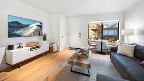 A modern living room with a wooden coffee table, a grey sofa, and a large window offering a view of a balcony. - West Side Chic: A Light & Bright Ski Retreat (Telluride)
