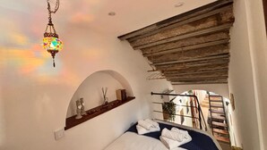 A bedroom with a bed, a hanging lamp, a wooden slat-covered window, and a small shelf with decorative items. - Cozy in the historic center of Palermo 300mt from the train station (Palermo)