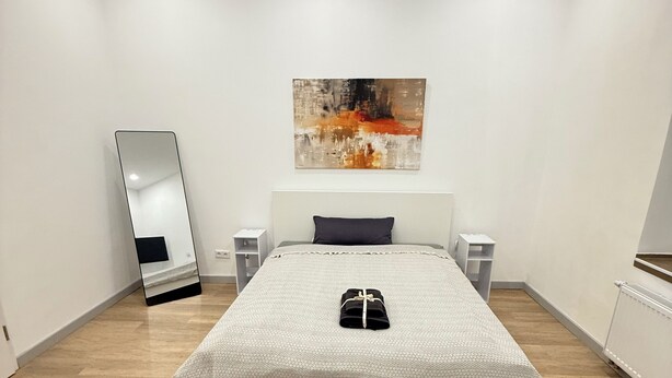 Camera da letto moderna con un letto grande, un quadro sopra il letto, uno specchio al muro e un termosifone a destra.