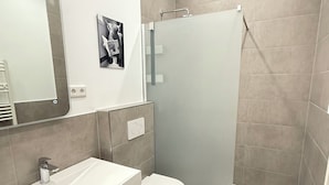 Un bagno moderno con un mobile lavabo bianco, un water, un box doccia e uno specchio.