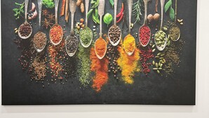 Un'opera d'arte appesa al muro raffigura cucchiai con diverse spezie ed erbe aromatiche.