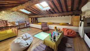 Une pièce mansardée chaleureuse avec un plafond en pente, des poutres en bois, un mur en pierre et une lucarne.