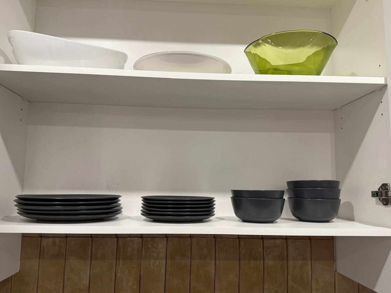 Uno scaffale da cucina con piatti bianchi e neri, ciotole e una ciotola di vetro verde.