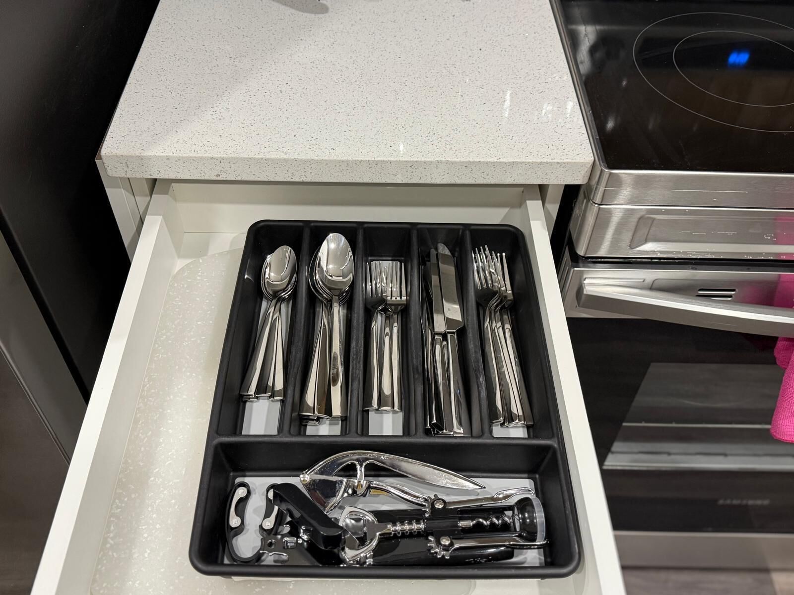 A drawer containing a set of silverware, including spoons, forks, and a bottle opener.