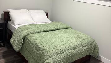 A bedroom with a bed, a nightstand, a window with blinds, and wooden flooring.