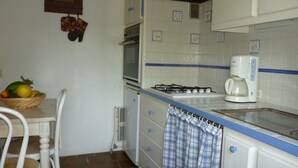 A kitchen with white cabinets, a stove, a coffee maker, and a fruit basket on the table.