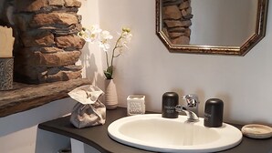 A bathroom with a stone wall, a white sink, a mirror, and a wicker basket.