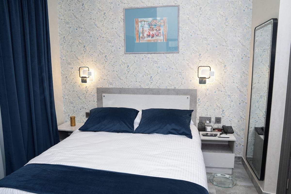 A neatly arranged hotel room with a bed, bedside tables, a desk, and a mirror.