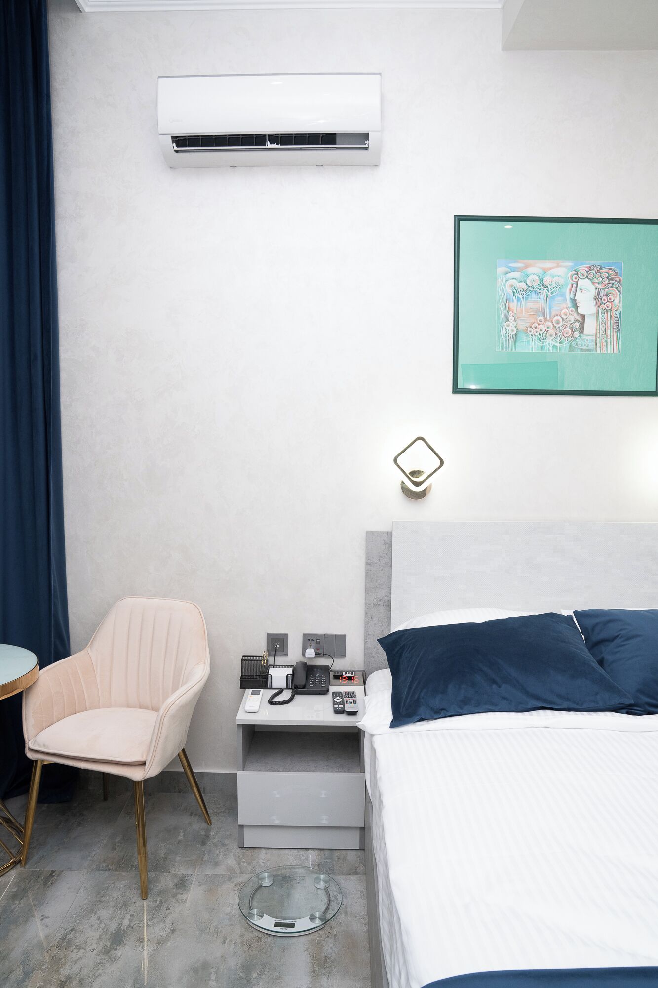 Habitación de hotel moderna con cama, una silla, un escritorio con teléfono y lámpara, y aire acondicionado en la pared.
