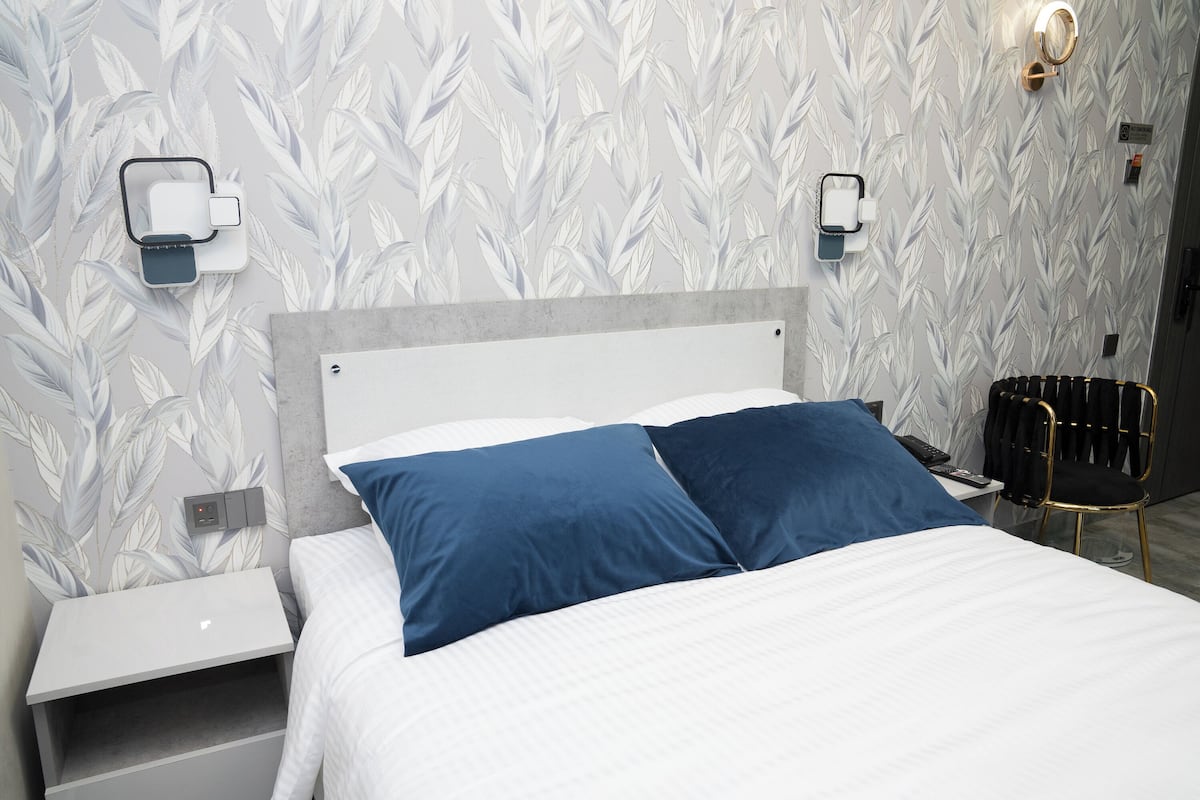 A neatly made bed with two pillows, a bedside table, a chair, and a wall-mounted light fixture.