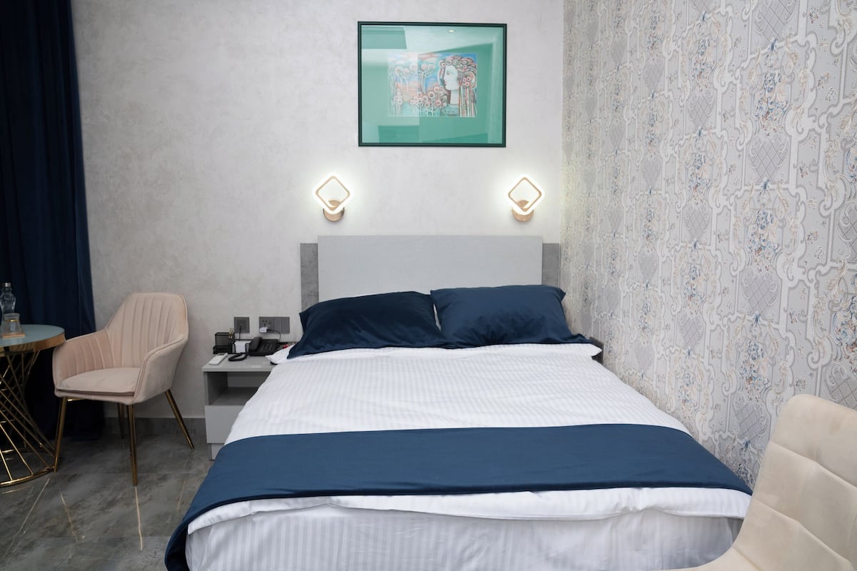A hotel room with a bed, a desk, a chair, and a wall-mounted artwork.