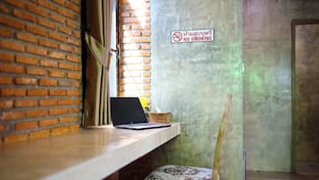 Una computadora portátil sobre un escritorio de madera con un pared de ladrillo y un cartel de 'No Smoking'.