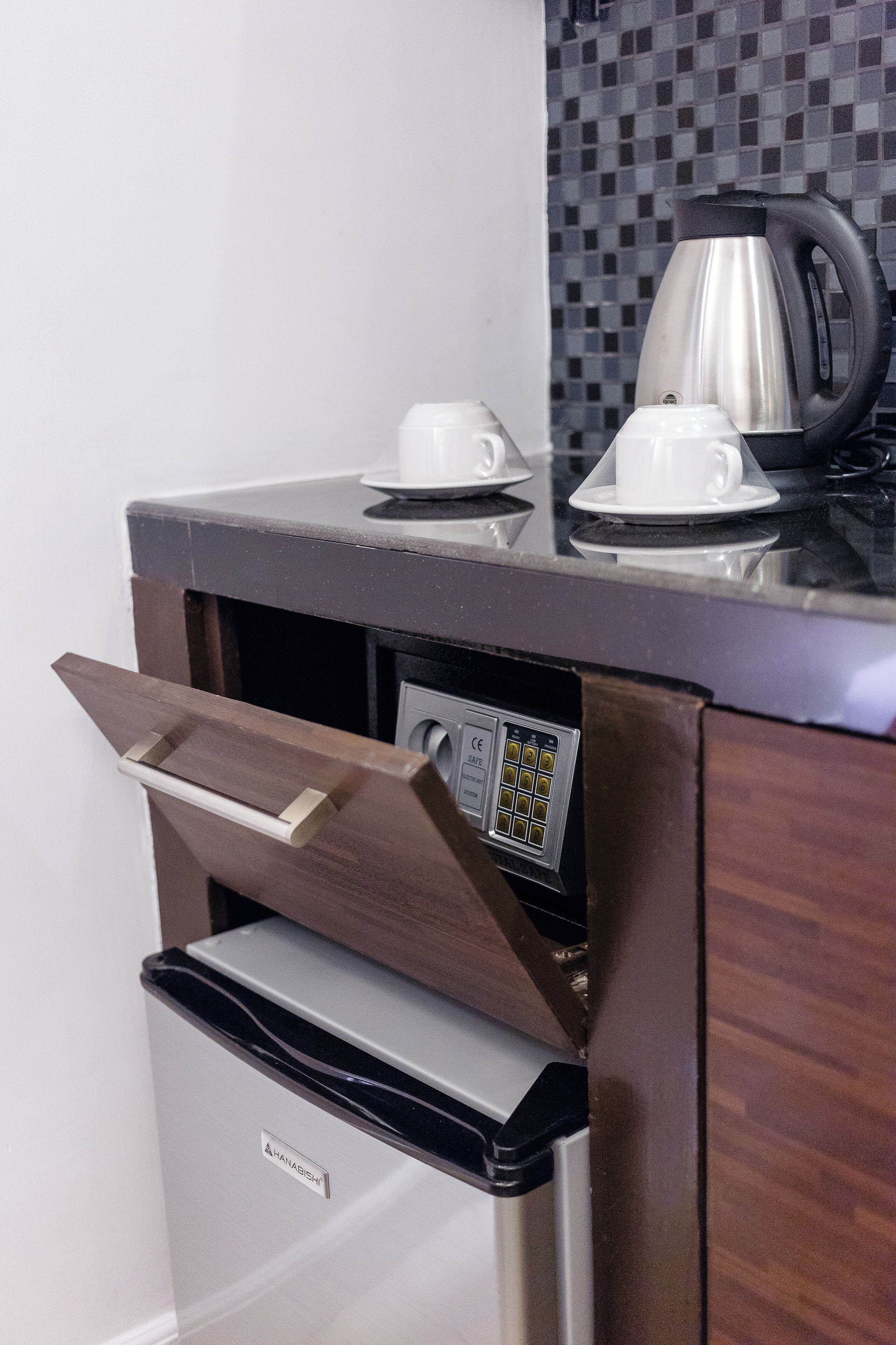 A compact kitchenette with a coffee maker, a cup, and a kettle on the counter.