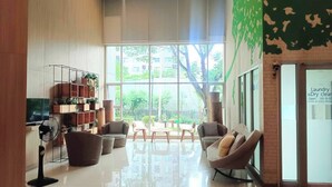 A spacious lobby with a large window, a television, a fan, and a wall-mounted shelf with plants.