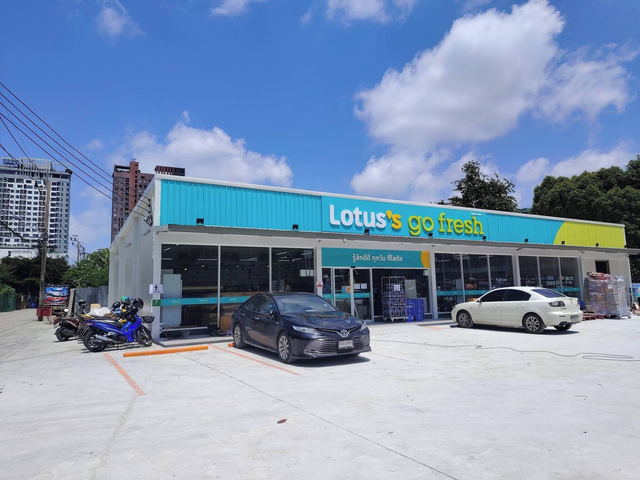 A Lotus's go fresh store with a blue and yellow facade, parking spaces, and a clear sky.