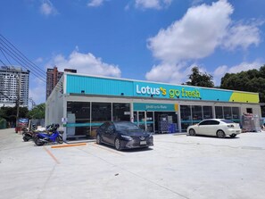 A Lotus's go fresh store with a blue and yellow facade, parking spaces, and a clear sky. - 1 BR 5 Mins BTS Bearing 7-11 and Lotus (Samut Prakan)