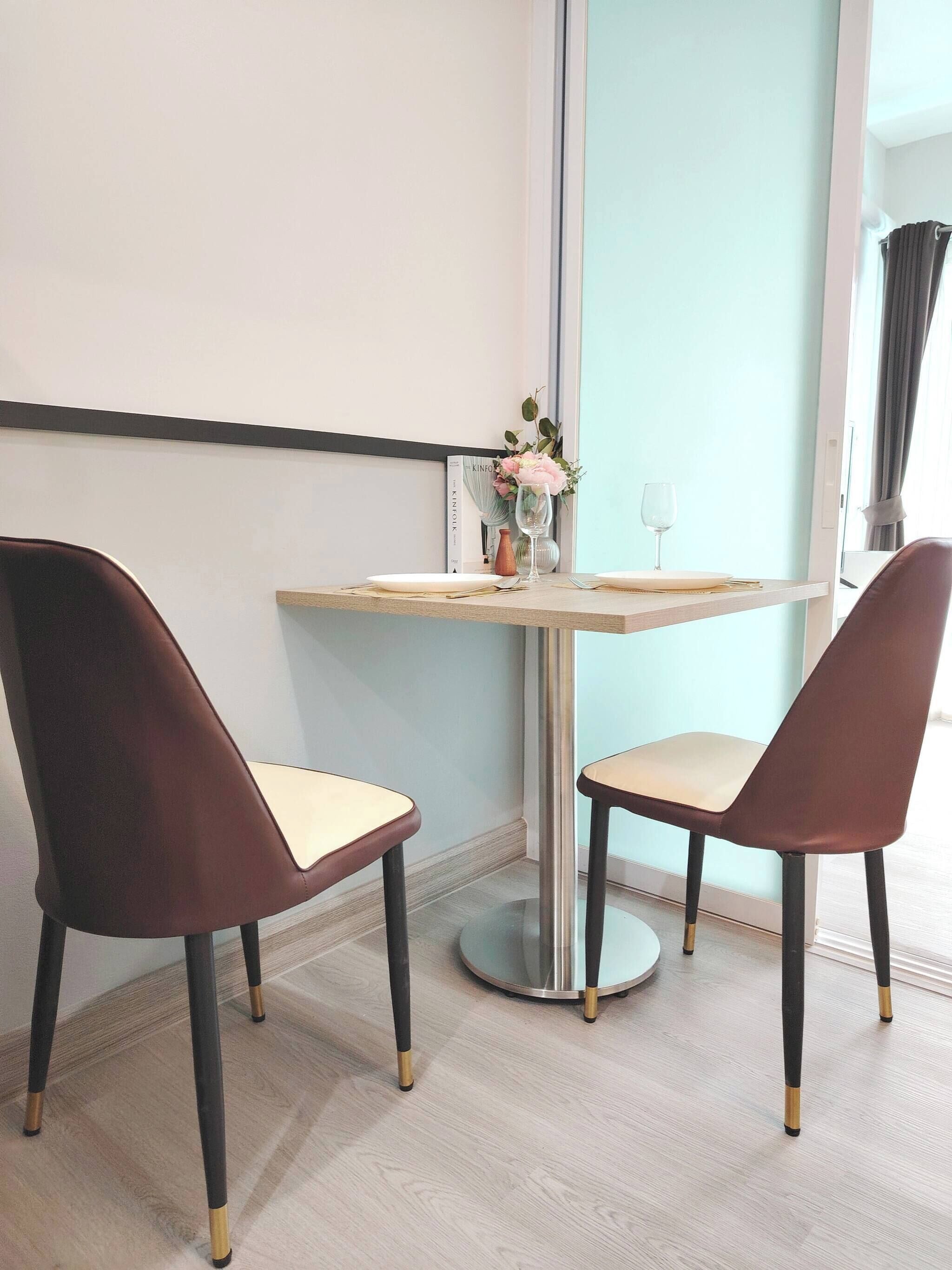 A modern room with a round table, two chairs, a vase with flowers, and a book on the wall.