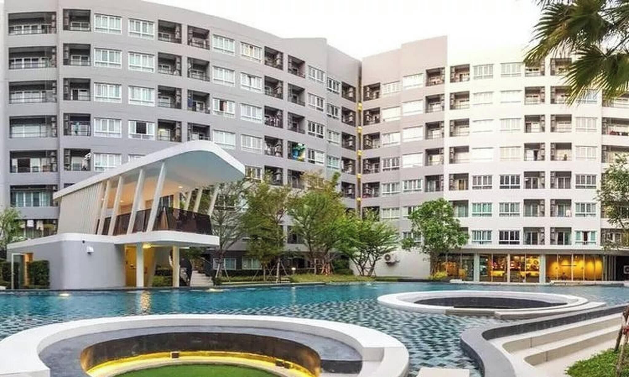 A modern hotel with a pool area, including a unique building with a curved roof and a circular water feature.