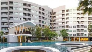 Un hotel moderno con zona de piscina, que incluye un edificio singular con techo curvo y una fuente circular.