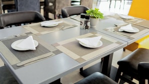 Una mesa de comedor dispuesta con manteles individuales, platos, cubiertos y una planta en maceta.