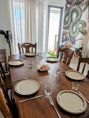A dining table set with plates, glasses, and cutlery, with a mural on the wall and a window with curtains.