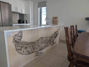 Une cuisine ornée d’une grande fresque représentant un crocodile, dotée d’un réfrigérateur en acier inoxydable et d’une table à manger en bois.
