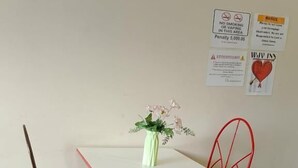 A small dining area with a white table and red chairs, a vase with flowers, and a notice board with various signs. - WJV INN CASUNTINGAN (Mandaue)