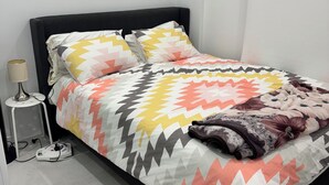 Un lit bien fait, recouvert d’une couvre-lit à motifs, une table de chevet avec une lampe et une œuvre d’art accrochée au mur.