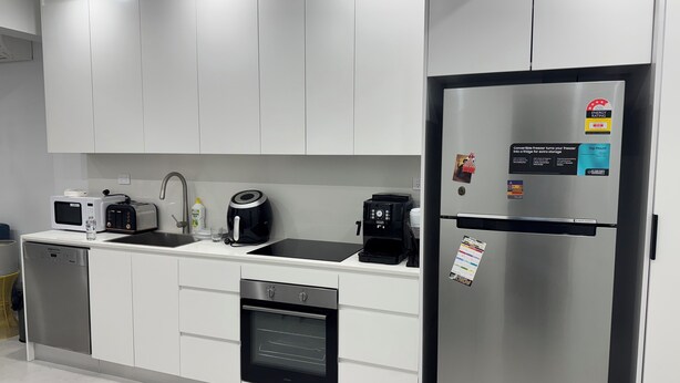 Une cuisine moderne avec des armoires blanches, un réfrigérateur en acier inoxydable, un four encastré, une machine à café et un four à micro-ondes.