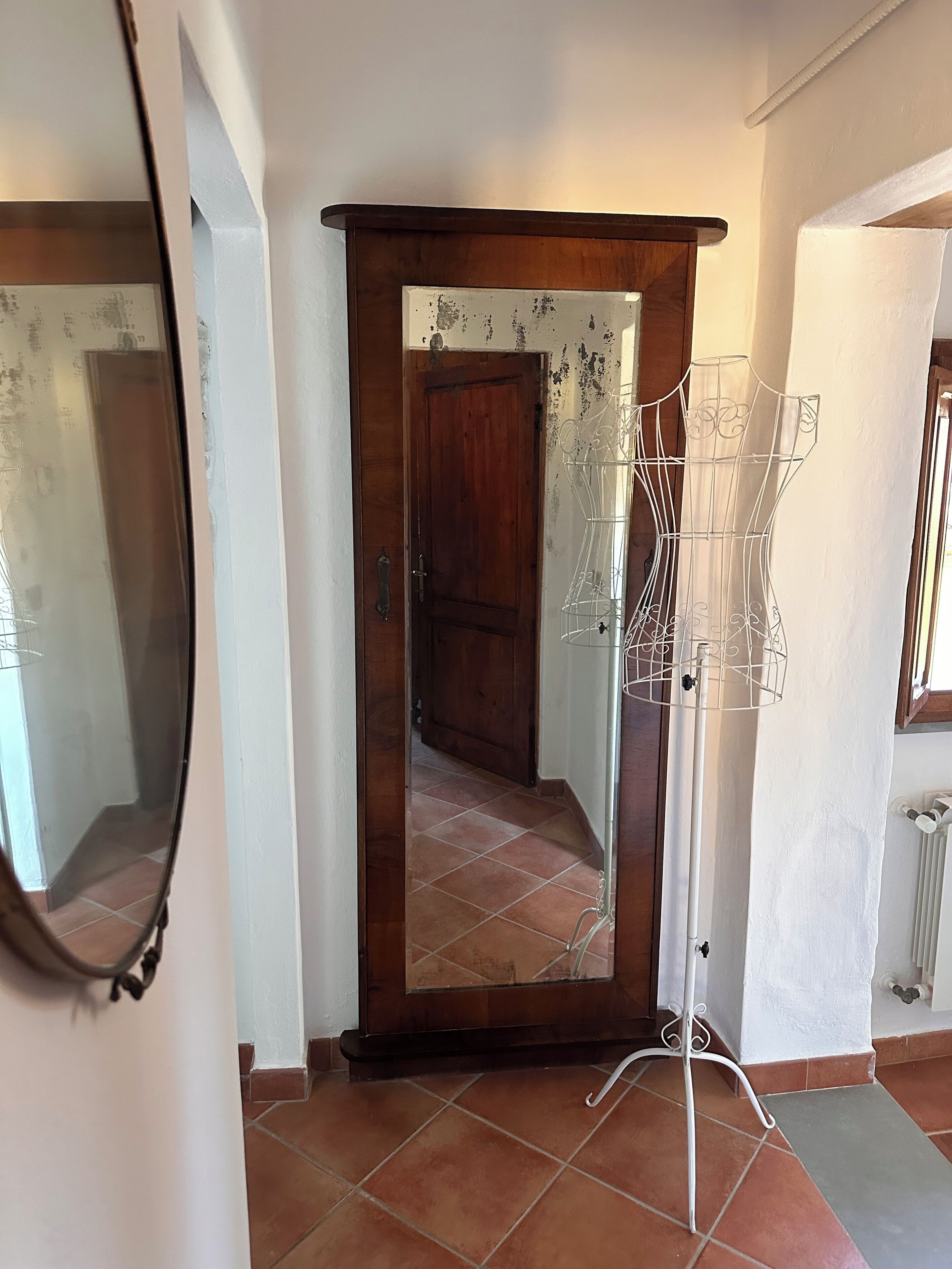 A hallway with a wooden door, a mirror, and a white metal rack.