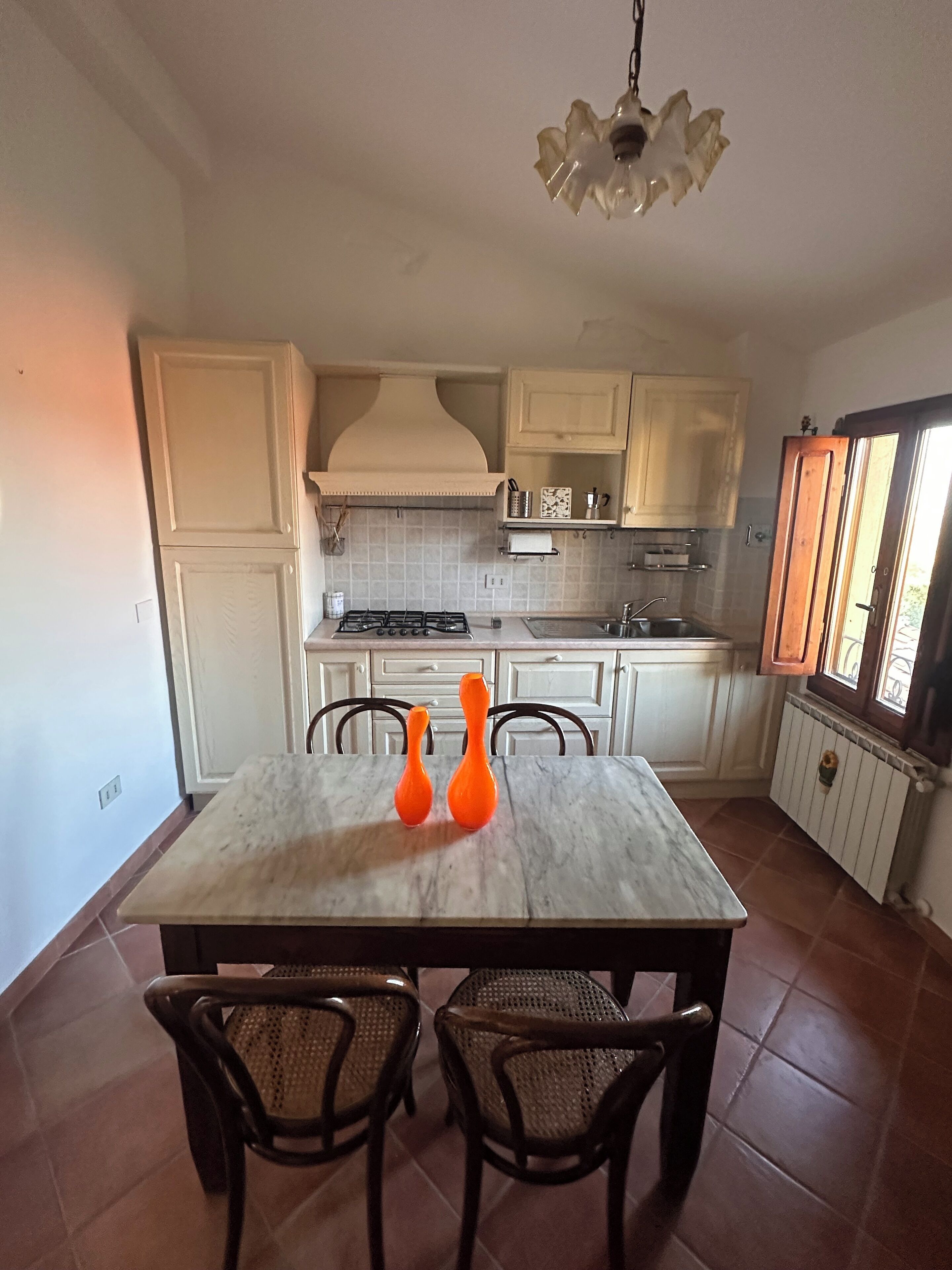 A kitchen with white cabinets, a stove, and two orange vases on the table.