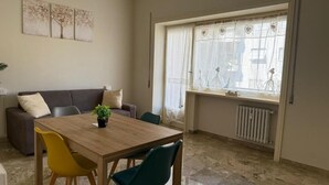 A dining area with a wooden table, yellow and teal chairs, a gray sofa, and a window with heart-shaped curtains. - MaSa Holidays House Vatican (Roma)