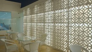 A modern outdoor seating area with white wicker chairs and a glass table, separated by a decorative white lattice wall. - Knightz bridge (Faizabad)