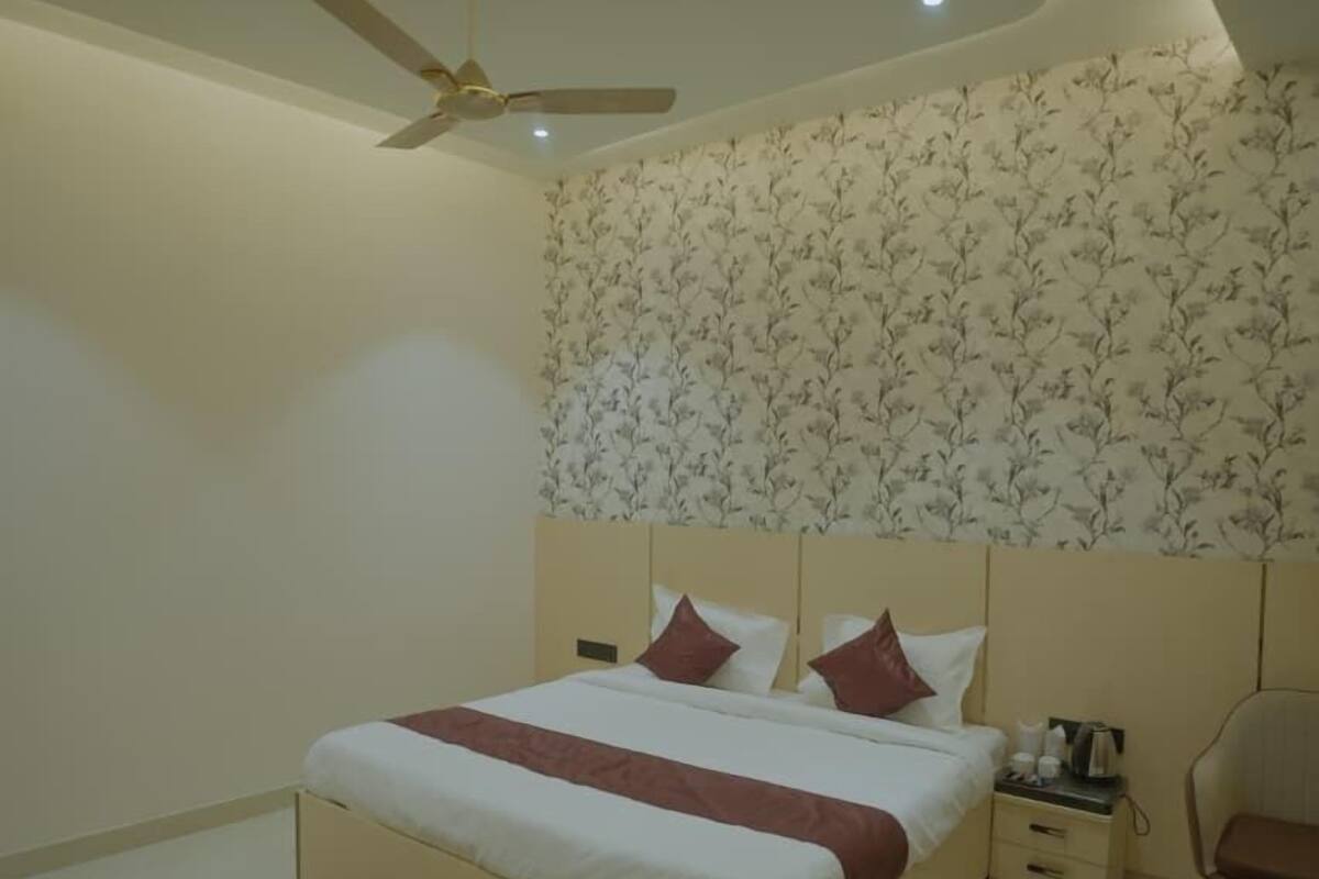 A bedroom with a bed, a nightstand, a chair, a ceiling fan, and a patterned wallpaper.