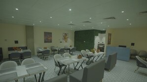 A hotel dining area with multiple tables and chairs, a reception desk, and a green accent wall. - Knightz bridge (Faizabad)