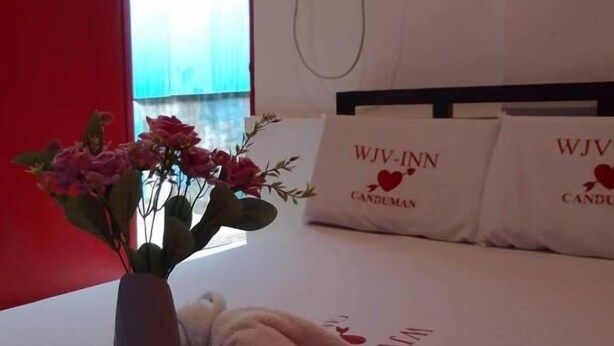 A hotel room with a bed, a vase of flowers, and pillows with the text "WJV-INN CANDUMAN". - WJV INN CANDUMAN (Mandaue)