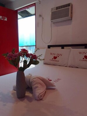 A hotel room with a bed, a vase of flowers, and pillows with the text "WJV-INN CANDUMAN". - WJV INN CANDUMAN (Mandaue)