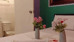 A hotel room with a bed, two vases with flowers, a painting on the wall, and a sign with the hotel name. - WJV INN CANDUMAN (Mandaue)