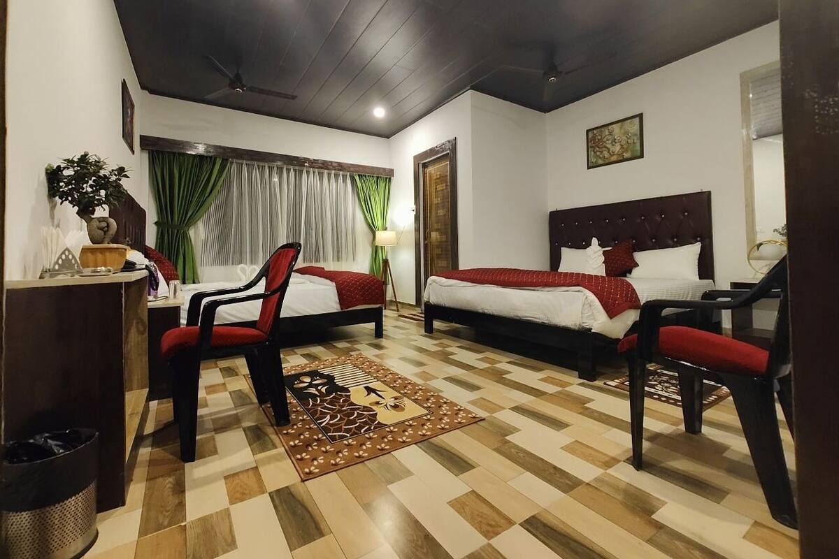 Una habitación de hotel con dos camas, un escritorio, sillas, piso a cuadros y un ventilador de techo.