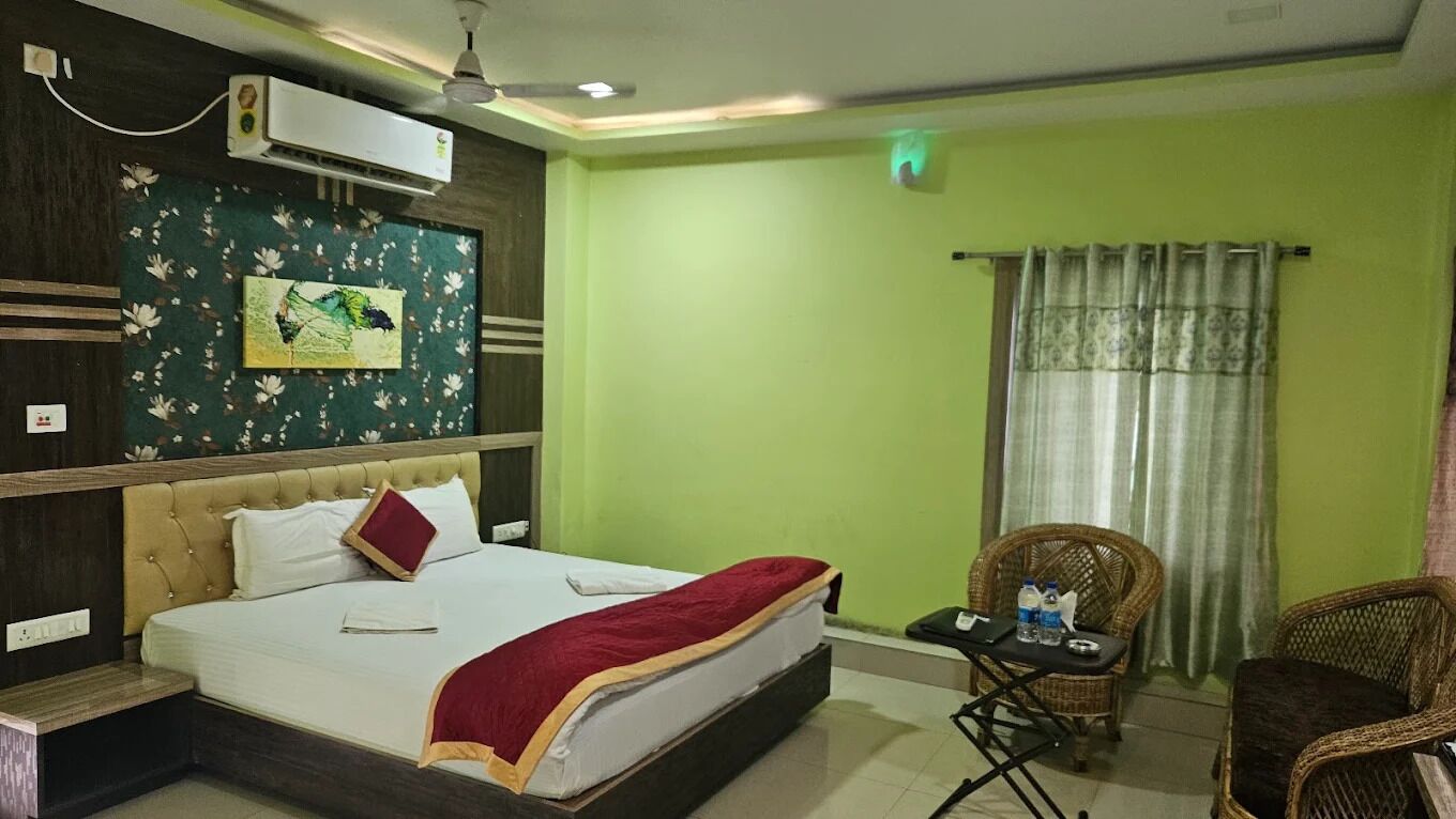 A hotel room with a bed, a chair, an air conditioning unit, and a wall-mounted artwork.