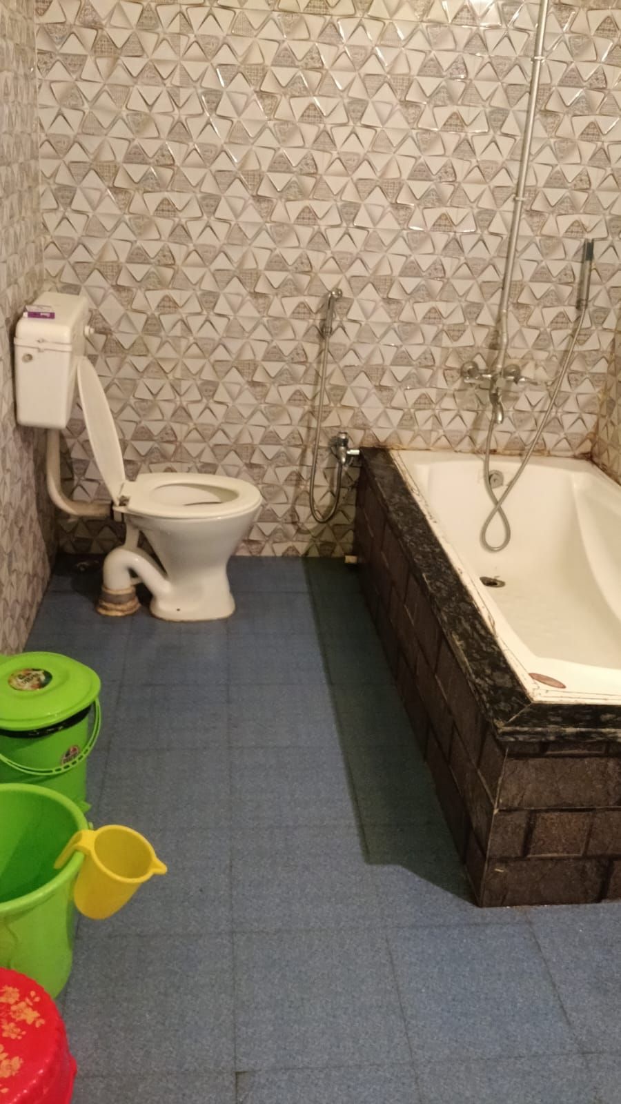 Une salle de bain avec des toilettes, une baignoire et une douche. On peut voir des seaux verts et jaunes sur le sol.