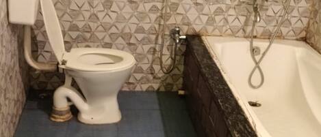 Une salle de bain avec des toilettes, une baignoire et une douche. On peut voir des seaux verts et jaunes sur le sol.
