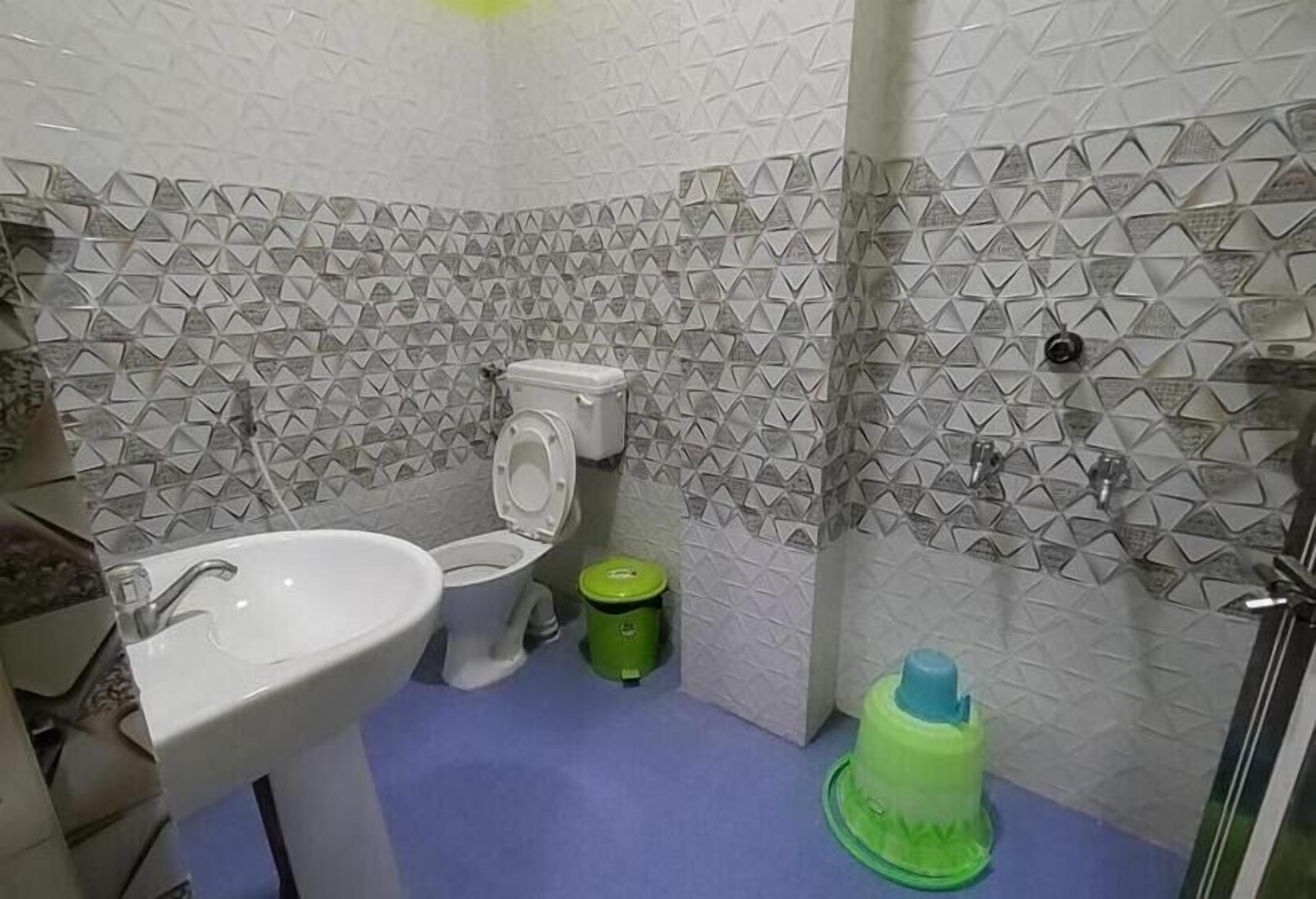 A bathroom with a white toilet, a sink, and a green trash bin.