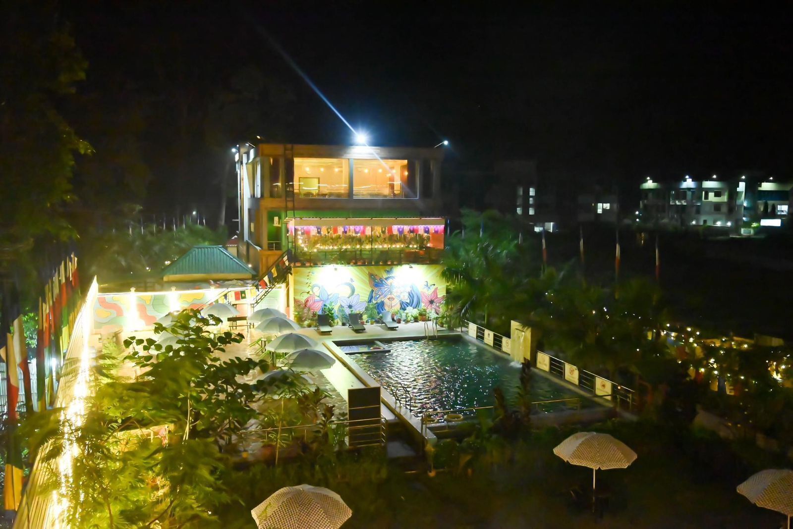 A hotel with a pool, outdoor seating, and a brightly lit entrance.