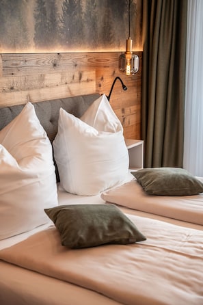 A bedroom with a wooden headboard, two beds, white and green pillows, and a wall-mounted light fixture.