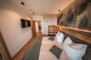 A hotel room with a bed, a TV mounted on the wall, and a painting of trees.